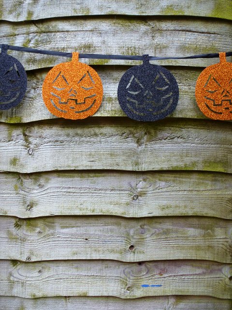 Orange and blue glitter pumpkin face garland for celebrating Halloween strung on a rustic wooden wall with copy space