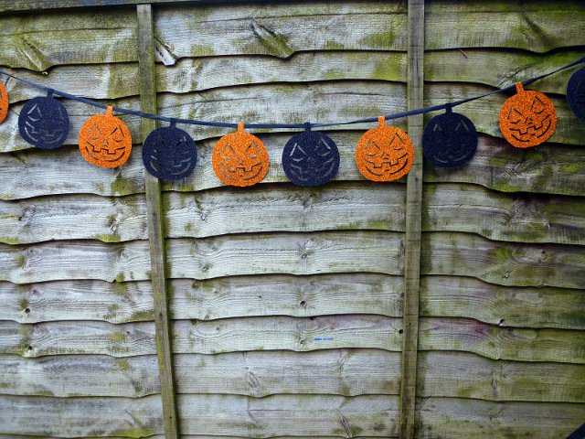 Decorative Halloween garland of glitter pumpkin faces hanging on an old rustic weathered wooden wall with copy space
