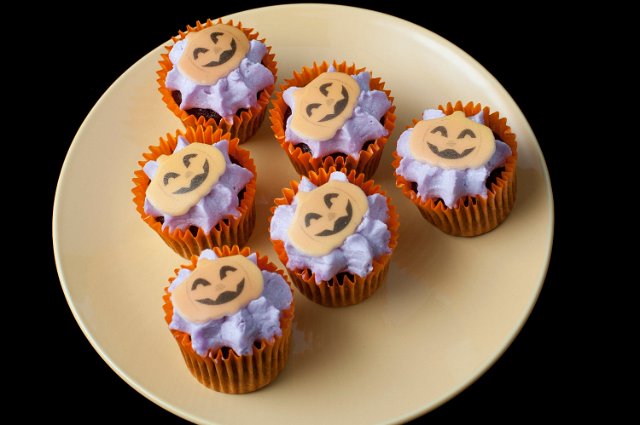 a plate with some halloween decorated iced mini cup cakes