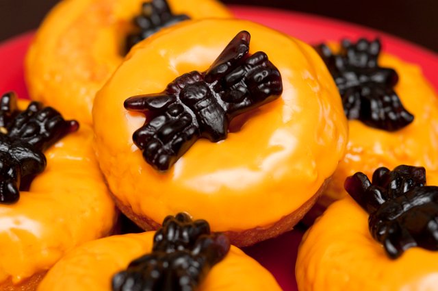 Closeup view of colourful orange frosted doughnuts topped with scary black jelly spiders for a Hallowween party or trick or treat