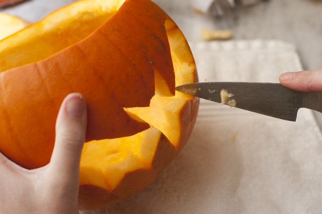 Man carving a pumpkin lantern for Halloween using a sharp kitchen knife to cut out the pattern of a flying bat from the hollowed out vegetable