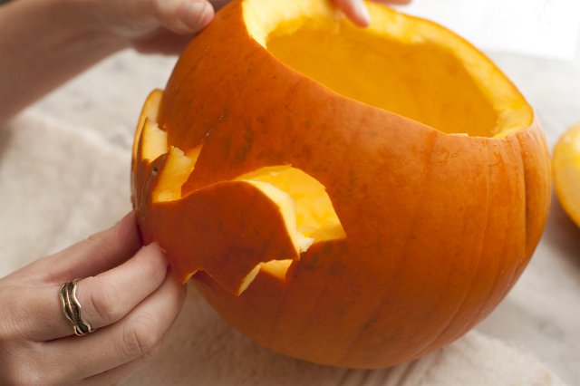 Carving a pumpkin for a Halloween lantern with a hand removing the cut out shape of a flying bat through which the candlelight will shine