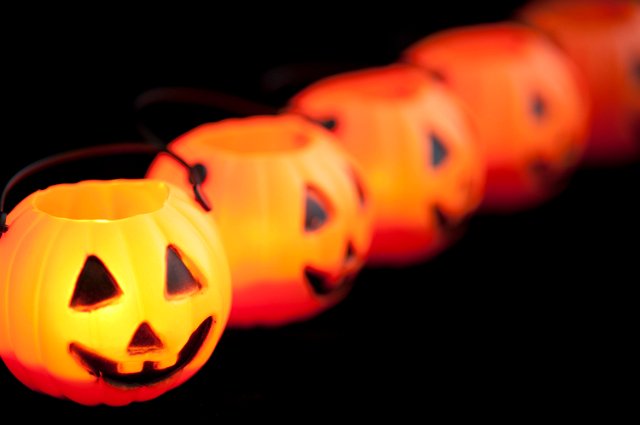 Row of creepy Halloween lantern ornaments arranged in a diagonal receding row with focus to the first lantern on the left, over a dark background