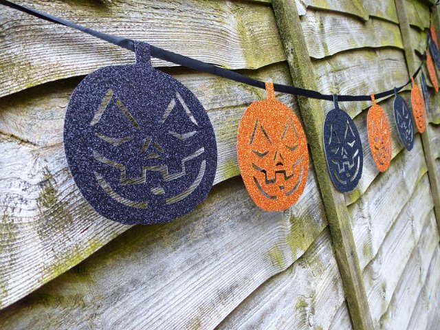 Halloween pumpkin garland of blue and orange colors, hanging on old wooden wall outdoors. Viewed from the side in close-up and in perspective
