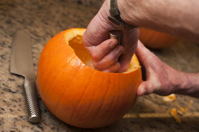 Man hollowing out a fresh pumpkin to make a traditional lantern or Jack-o-lantern for Halloween festivities