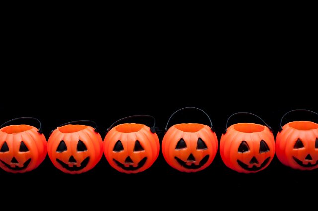 Row of orange ceramic Halloween pumpkin lantern ornaments on a dark background forming a border with plenty of copyspace for your greeting or invitation