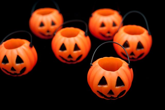 Group of orange ceramic pumpkin jack-o-lantern ornaments with cut out faces and handles on a black background
