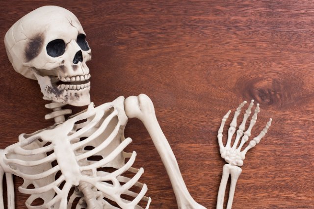 a waving halloween skeleton decoration on a natural wood backdrop with space for text