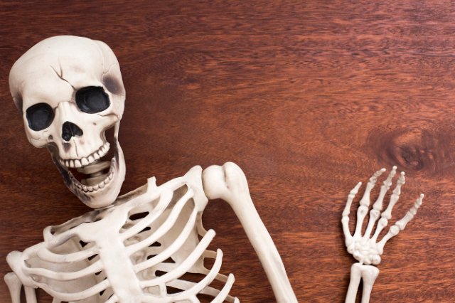 a laughing halloween skeleton decoration waving a hand with wooden background