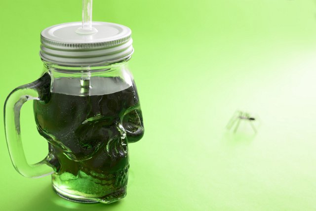 Green Halloween drink in a skull shaped glass mason jar with lid and straw over a graduated background with copy space