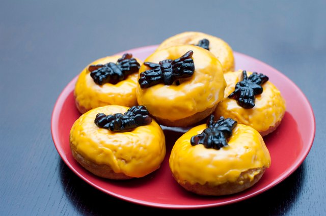 Plate of Halloween doughnuts with colourful orange icing and black jelly spiders for a creepy trick and treat