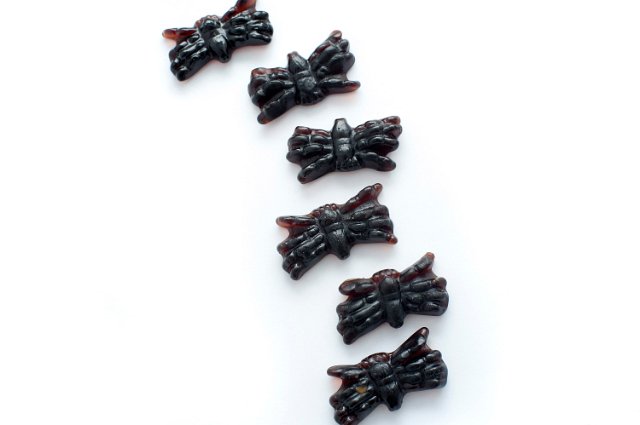 Black spooky Halloween spider candy made of jelly arranged in a vertical row on a white background with copyspace