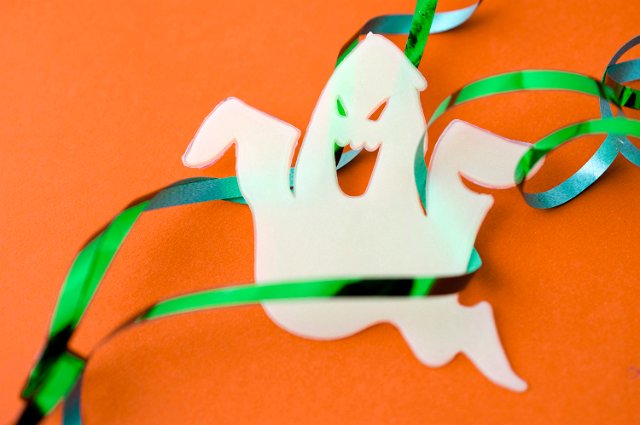 Spooky white Halloween ghost decoration with green foil party streamers on an orange background with copyspace