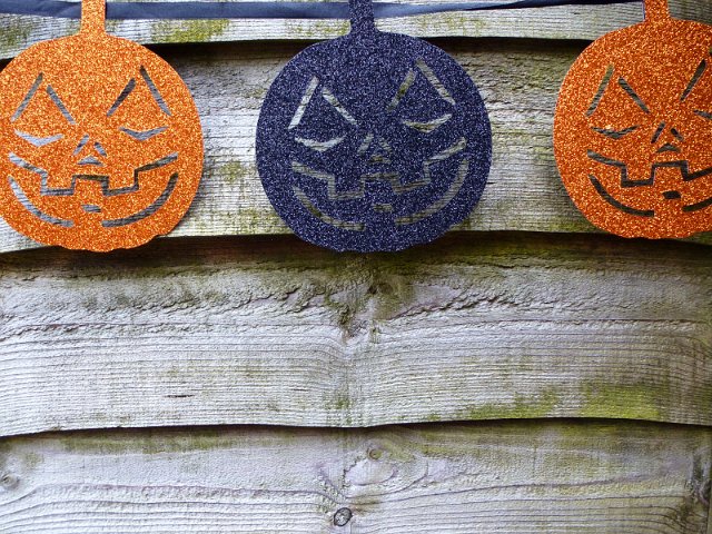 Rustic Halloween background with colorful glitter pumpkin faces on a string hanging on a wooden wall with copy space