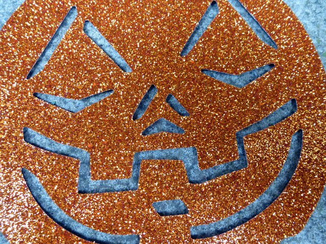 Grinning evil pumpkin face decoration in orange glitter to celebrate the Halloween festival in a close up background texture