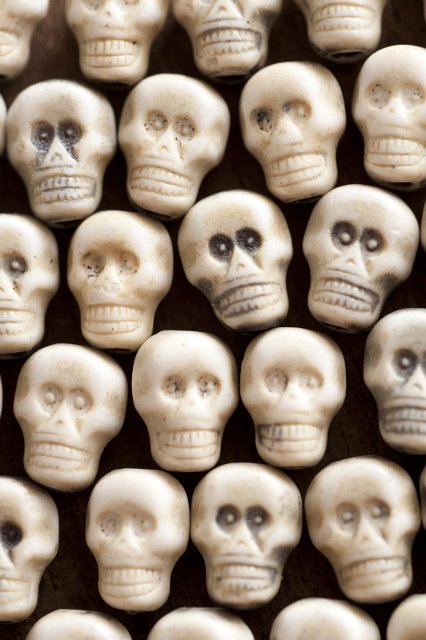 Macabre ghoulish Halloween skull background with a densely packed arrangement of white toy skulls on black in an overhead full frame view