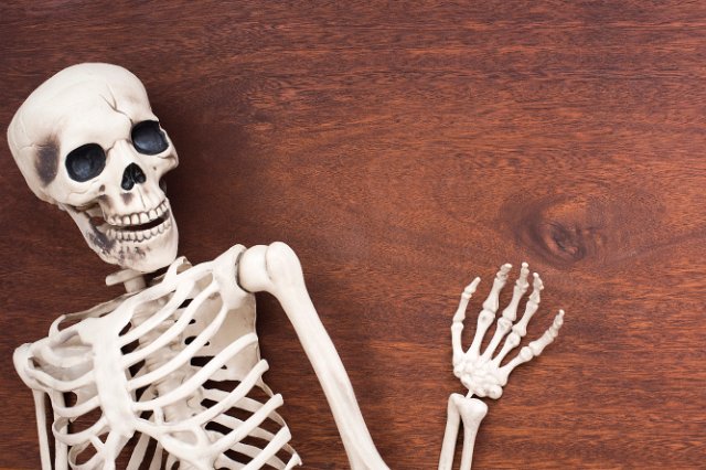 a happy looking halloween skeleton decoration with waving hand on a natural wooden surface